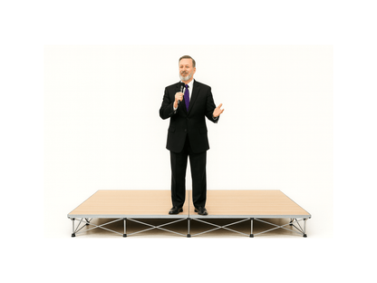 Man in a suit standing on a LimeLight Lite Series 8x8 modular stage platform in Wood Laminate at 8" height. Ideal for schools, churches, and event professionals.